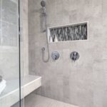 A gray-tiled walk-in shower contains a bench with a white towel and a gray washcloth. There's a window in the shower.