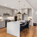 A modern kitchen with white counter tops, stainless steel appliances, and hardwood floors next to an entry hallway.