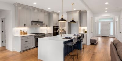 A modern kitchen with white counter tops, stainless steel appliances, and hardwood floors next to an entry hallway.
