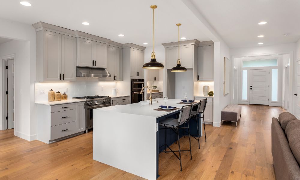 A modern kitchen with white counter tops, stainless steel appliances, and hardwood floors next to an entry hallway.