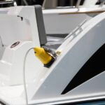 A white electric boat sits in the marina, receiving an electric charge from a bright yellow charger.