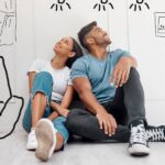 A young couple sitting on the floor with sketches of possible home customizations around them thinking about improvements.