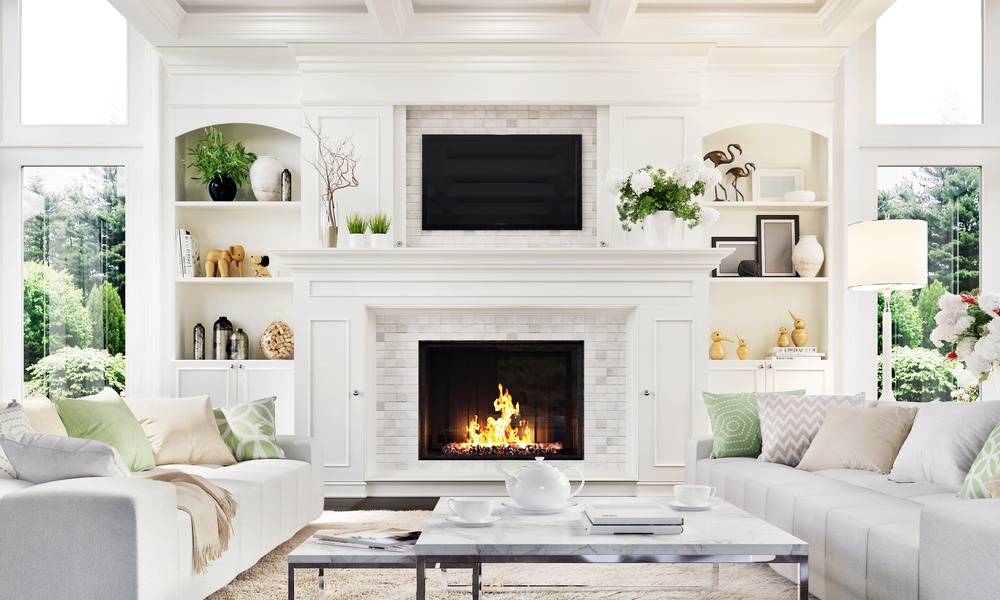A luxurious home living room with a large fireplace in the center surrounded by white accents, decor, and furniture.