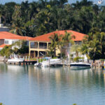 A neighborhood of luxury waterfront homes with palm trees in the homes' backyards, and boat docks in their front yards.