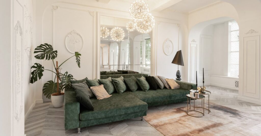 A green couch faces forward with a mirror behind it, set against white walls and gray parquet flooring with a brown rug.