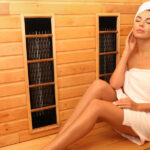A woman with a white towel wrapped around her body and a white towel wrapped around her head sits in a sauna.