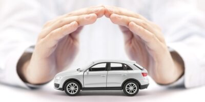 A close-up view shows a small, white toy SUV sitting on a white surface with a pair of hands forming a cover over it.