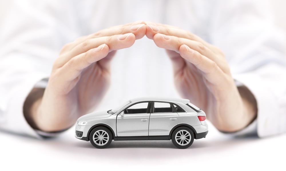 A close-up view shows a small, white toy SUV sitting on a white surface with a pair of hands forming a cover over it.