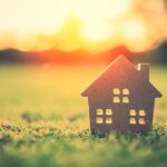 Things To Look For in a Summer Home Property A small, wooden model of a house sitting on a patch of green grass with a sun setting in the background.