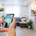Unexpected Ways To Incorporate Smart Home Technology A hand holding a smartphone about to press a lock button in their home's living room. The phone reads "smart home".