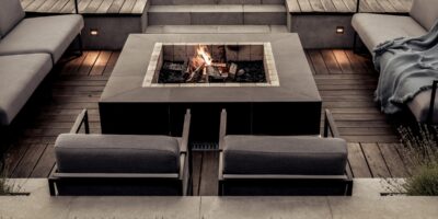 Gray stone steps lead to a sunken patio with a lit fire pit, metal seating, and distressed wooden flooring.